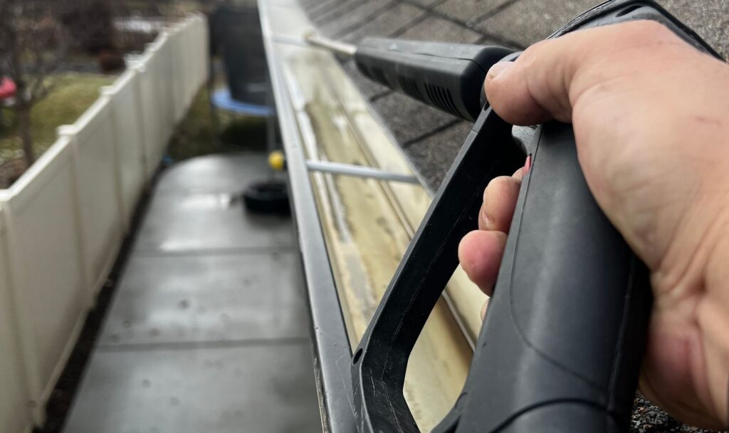 Close-up of residential gutter cleaning in progress beside an asphalt shingle roof