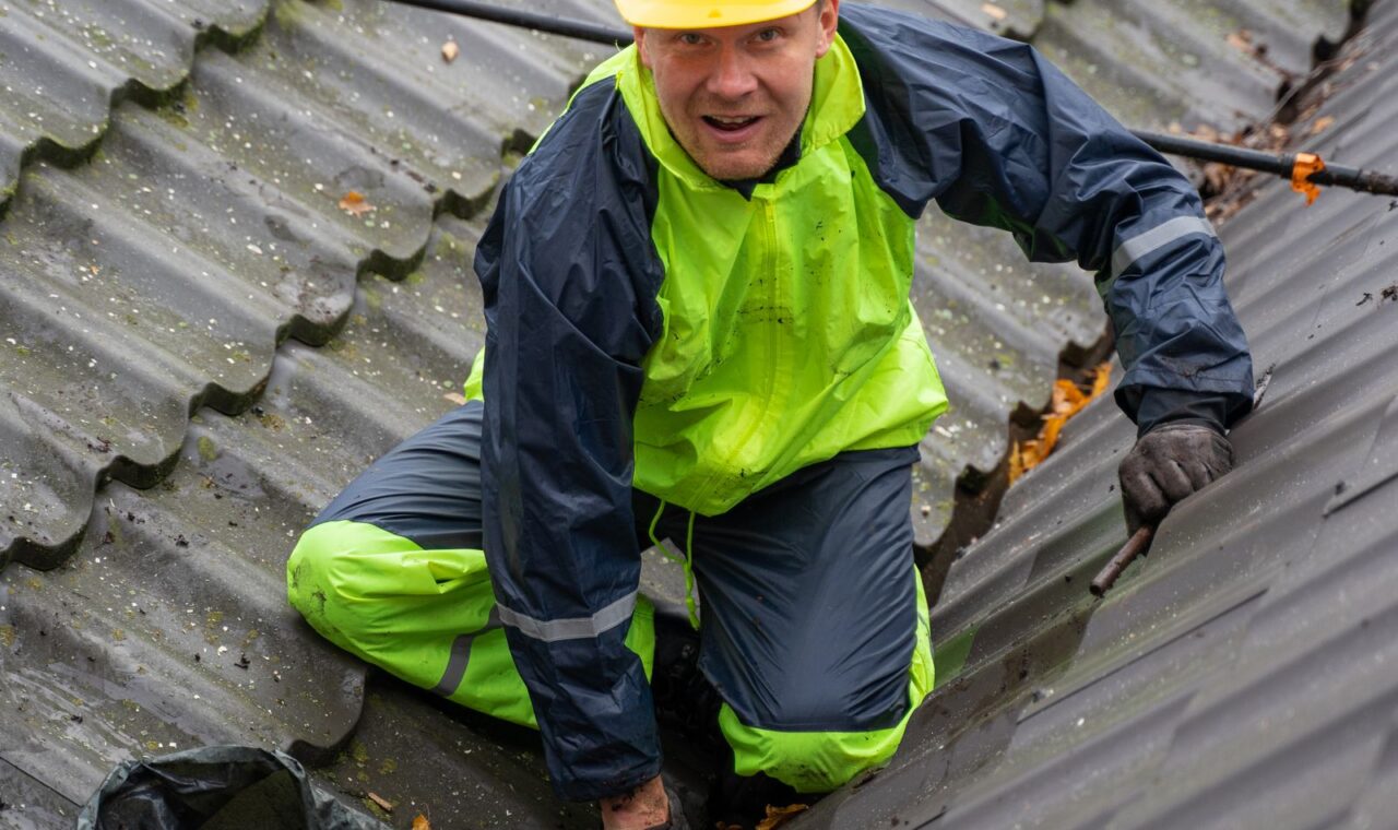 Roof-care professional working on a residential roof in wet-weather gear